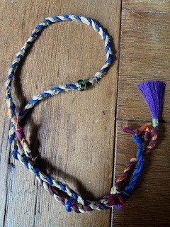 a blue and white and purple sari silk cordage necklace with beads rests on an old redwood table.